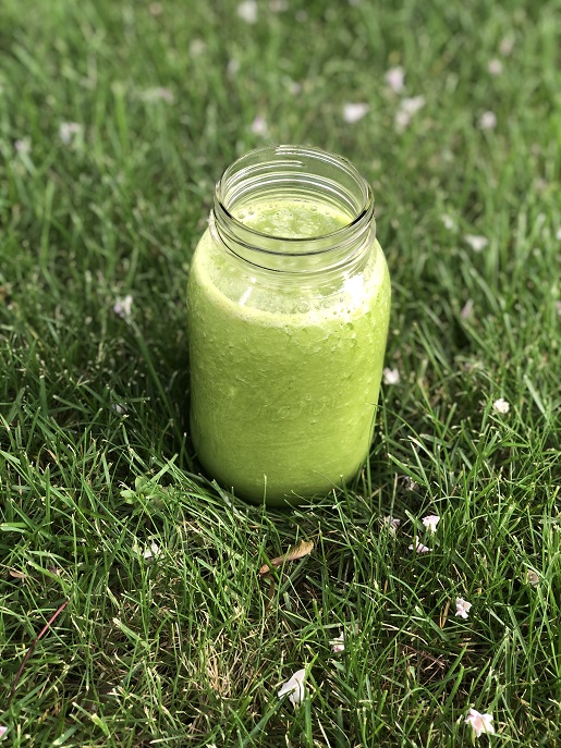 green smoothie in a jar on the grass surrounded by small white flowers